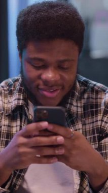 Etrafında şık ve çağdaş bir ev ortamında akıllı telefonuna odaklanmış genç bir adam.