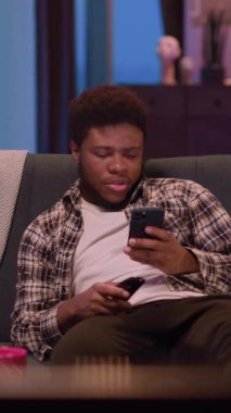 Genç bir adam rahat bir şekilde kanepede uzanıyor, rahat ve davetkar bir ortamda akıllı telefonuna odaklanmış.