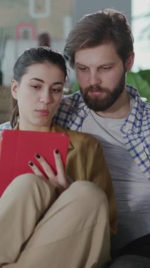 Kafkasyalı çift Tablet Bilgisayar kullanarak evde kalıyor. Genç Evli Adam ve Kadın İnternetten Alışveriş Yapıyor Not Defteri Uygulaması Oturma Odasında Kullanılıyor.