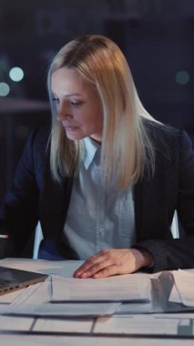 Genç, yetişkin bir iş kadını dizüstü bilgisayar kullanıyor ve evrak işleriyle uğraşıyor. Kurumsal işlerle boğuşan kadın ofiste uzun süre çalışıyor..