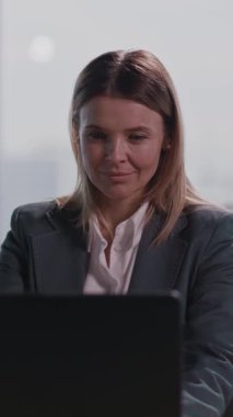 Profesyonel bir kadın masasında oturmuş laptopuna özgüvenle odaklanmış modern iş ve profesyonelliği çağdaş bir ofiste somutlaştırıyor.