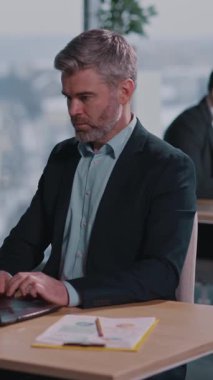 Takım elbiseli profesyonel bir adam masadaki bilgisayarına bağlanır, üretkenliğini gösterir ve sofistike bir atmosfere odaklanır.