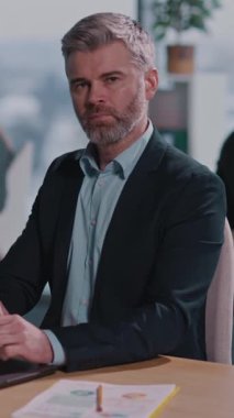 Takım elbiseli ve mavi gömlekli bir adam modern bir ofiste dizüstü bilgisayarına odaklanmış, kurumsal hayattaki konsantrasyonunu ve kararlılığını gösteriyor.