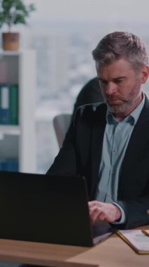 Profesyonel bir sahnede takım elbiseli bir adam dizüstü bilgisayarla çalışıyor, sonra ona ve evrakları inceleyen, takım çalışmasına dikkat çeken bir kadına geçiyor.