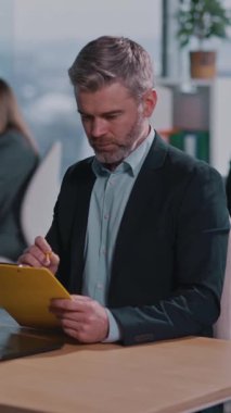 Profesyonel bir ofiste, iyi giyimli bir adam masasında çalışkanlık ve coşkuyu dengeleyen, profesyonellik ve organizasyon sergileyen görevler yapar.