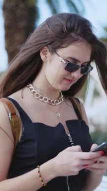 Plajda palmiye ağaçlarının arka planında yürüyen cep telefonlu beyaz bir kadın. Yaz manzarası. Güzel insanlar..