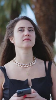 Şık, genç, kaygısız bir kadın cep telefonu kullanıyor sosyal medyada mesajlar yazıyor şehir plajında yürüyüş yapmanın keyfini çıkarıyor..