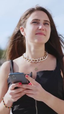 Zarif elbiseli güzel bir bayan turist cep telefonu kullanıyor sosyal medyada gezinen mesajlar atıyor. Palmiye ağaçları. Deniz manzarası. Turizm konsepti.