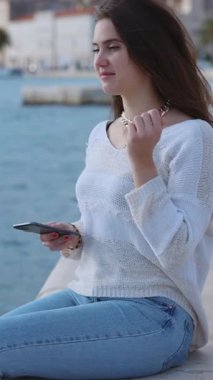 Mutlu ypung kadını rıhtımda oturmuş açık havada güneşli bir günde kulaklıkla favori müzik parçalarını dinliyor..