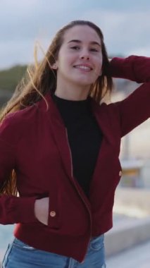 Sahilde yürüyen harika saçlı neşeli genç kız kameraya neşeyle gülümsüyor. Yaz zamanı. Denize açılın. Turizm konsepti.