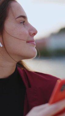 Akıllı telefonlu beyaz bir kadın açık havada sinemada kalan kulaklık takıp müzik listesindeki favori şarkıları dinliyor. Tatil kavramı.