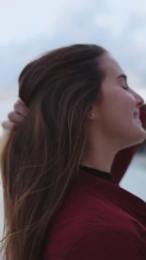 Sahil şeridi boyunca yürüyen çekici, genç ve modern bir kadın. Gün batımının tadını çıkarıyor. Kameraya gülümsüyor. Açık hava portresi. Turizm konsepti.