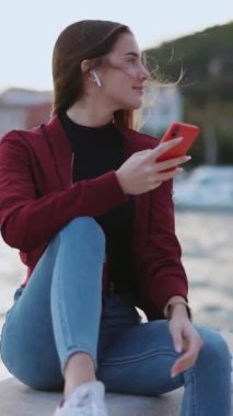 Güzel bir yaz günü, genç bir kadın şehir sahil şeridinde oturan akıllı telefon uygulaması ile kulaklıkla müzik dinliyor..