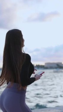 Spor giyimli aktif genç bir bayan güzel bir yaz akşamında sahil şeridinde cadde boyunca koşuyor. Sağlıklı bir yaşam tarzı. Spor dünyasındaki insanlar. Teknoloji.