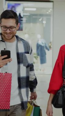 Bu videoda şık bir alışveriş merkezinde alışveriş yapan, şık giyimli ve cep telefonlarıyla bağlanmış bir çift görülüyor. Özellikle kadınların kırmızı kazaklarını vurguluyorlar.