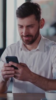 Video, akıllı telefonuyla meşgul bir adamı gösteriyor. Yeni şeyler keşfederken gülümsüyor, teknolojiyle neşe ve bağlantı kuruyor.