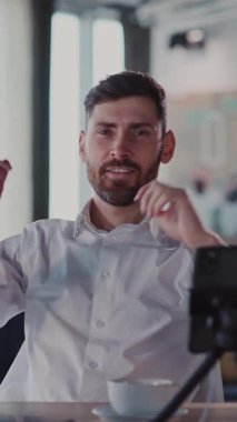 Bu videoda, sakallı bir adam bir kafede dinleniyor, kahveyi yudumluyor ve laptopunu kullanıyor, odak noktasını somutlaştırıyor ve beyaz kıyafetle gündelik keyfine bakıyor.