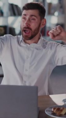 Beyaz gömlekli bir adam yemek ve dizüstü bilgisayarı olan bir masada oturuyor, konfor ve verimliliği somutlaştırıyor, dengeli bir modern yaşam tarzını yansıtıyor.