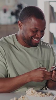 Neşeli bir adam telefonuna bakarken patlamış mısırla atıştırıyor, keyfine bakıyor. Mutluluk ve bağlılık saçan bir yemeğin tadını çıkarıyor.