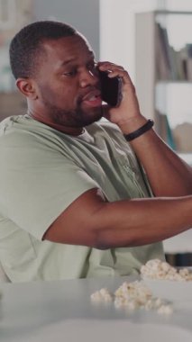 Bir adam masada oturmuş, patlamış mısırla rahat bir ortamda cep telefonuyla sohbet ediyor, ifadesiyle gevşemiş iletişimi somutlaştırıyor.