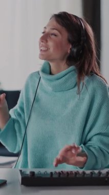 Mavi kazaklı bir kadın klavye ve kulaklıklarla bir masada oturur, müziğe dalmış, tutkusunu ve yaratıcılığını sergiler.