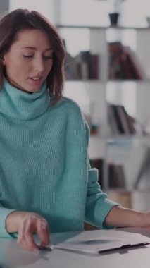 Mavi kazaklı bir kadın şık bir masada çalışıyor. Tablet ve dizüstü bilgisayar arasında gidip geliyor. Odaklanma ve verimliliğini gösteriyor.