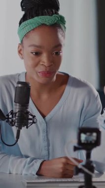 Masada oturan bir kadın düşünceli bir tartışmaya girer, mikrofona konuşur. Yeşil saç bandı ve rahat duruşu röportaj, podcast ya da hikâye anlatmak için ideal bir ortam yaratıyor.