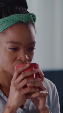 Yeşil bantlı neşeli bir kadın kahvesinin tadını çıkarıyor, kırmızı bir fincanla gülümsüyor, günlük mutluluğun neşeli anlarını yakalıyor.