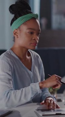 Video, yeşil bantlı, yaratıcı bir şekilde bir not defterine yazı yazan ve daha sonra tablet kullanan genç bir kadını canlandırıyor.