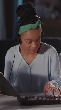 Bir kadın müzik ve teknoloji yeteneklerini yaratıcı bir oturumda sergiliyor, kulaklık takıyor, tablet ve klavyeyle etkileşime geçiyor, tutkusunu vurguluyor.