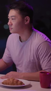 Mor gömlekli bir adam, sabahları kahve ve kruvasanla geçirir. Bilgisayarına odaklanmadan önce yemeğin tadını çıkarır.