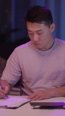 Odaklanmış bir adam rahat bir masada dizüstü bilgisayar ve panoyla çalışır, not almak, teknoloji ve geleneği harmanlamak için tablete geçer.