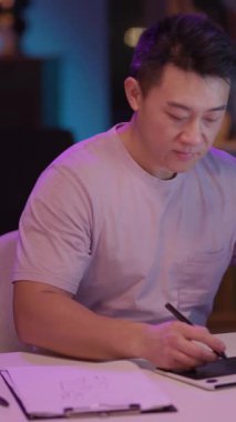 Sessiz bir ortamda, bir adam masada oturur, kollarını bağlar, notlar yazmak için tablet kullanır ya da tasarım yapar, yansıma ve nişanı dengeler.