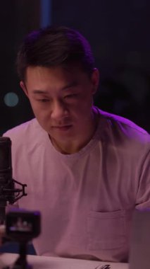 Mor gömlekli bir adam mikrofonlu bir masada oturuyor, panoya yazı yazıyor, önemli bir tartışmaya hazırlandığını öne sürüyor.