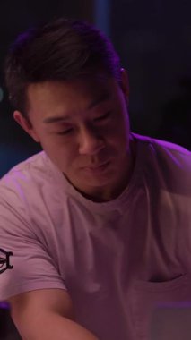 Bu video, pembe tişörtlü bir adamın dizüstü bilgisayara odaklanmış, mikrofon kullanan ve cep telefonuyla etkileşime giren bir adamı gösteriyor.