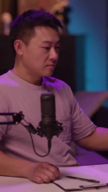 Bir adam düşünceli bir şekilde masada mikrofonla tartışıyor, kırmızı bardaktan yudumluyor, sezgilerini paylaştığı için davetkar bir atmosfer yaratıyor.