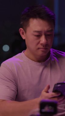 Mor renkli şık bir gömlek giymiş genç bir adam ekranında bir şey izlerken dikkatle cep telefonuna bakıyor.