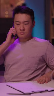 Bir adam cep telefonuyla konuşurken rahat bir şekilde masada oturuyor, muhtemelen önemli ya da sıradan bir şeyi tartışıyor.