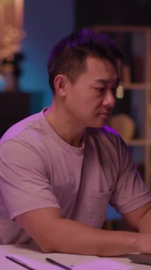 Mor gömlekli odaklanmış bir adam masadaki dizüstü bilgisayarında çalışır, kameraya bakar, konsantrasyonu ve verimliliği somutlaştırır.