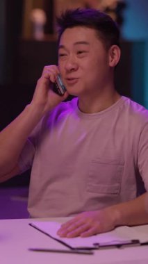 Masadaki bir adam mikrofon ve cep telefonu kullanıyor. Gülümsüyor ve arkadaş canlısı. Resmi olmayan ama profesyonel bir ortamda iletişim kuruyor.