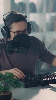 Kulaklık ve gözlüklü odaklanmış bir adam modern bir çalışma istasyonunda müzik prodüksiyonuna girişiyor ve sanatına olan bağlılığını ve tutkusunu sergiliyor.