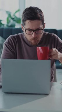 Bu video, odaklanmış gözlüklü bir adamı laptopunda özenle çalışırken gösteriyor. Verimliliği kahve molası anlarıyla dengeliyor.