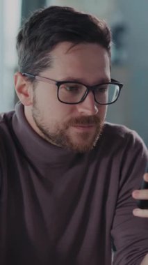 Bu videoda, şık bir balıkçı yaka giyen düşünceli bir adam akıllı telefonuyla iletişim kuruyor, başka bir adamla birlikte odak ve merak gösteriyor.