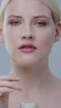 Güzellik rutinini vurgulayan, küçük, zarif bir kavanozdan cilt bakımı yapan bir kadının yakından görüntüsü.