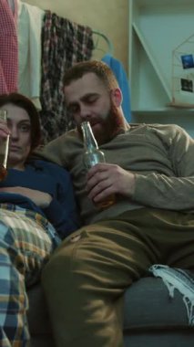 Alkolik genç çift bira içiyor. Kanepede oturuyor. Stresli, sağlıksız, ürkek, umutsuz, mutsuz, yetişkin alkolizmi.