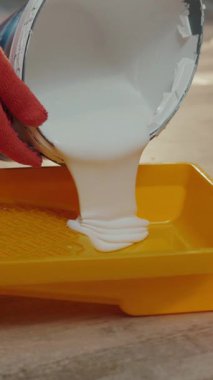 NEW YORK - 5 Nisan 2017: Turuncu koruyucu eldivenli bir inşaatçının elleri beyaz boyayı boya izlerine döküyor. Tamirat, yenileme, büyük tamirat. Aktif yaşam tarzı, yaşam biçimi. Yavaş çekim, kamera dengeleyici çekim