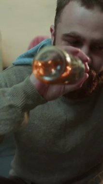 Kızgın genç bir kadın bağırıyor bir adama vuruyor bir alkolik kanepeye oturuyor bira içiyor üzgün stres, alkolik ev çaresiz alkol adam yorgun erkek şişe ağır çekimde portre yakın çekim