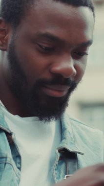 Dışarıda oturan sakallı bir adam akıllı telefonuna derinden odaklanır. Konsantrasyonunu ve nişanını gösterir.