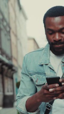 Odaklanmış bir adam bugün hareketli bir şehir ortamında yürürken akıllı telefonunu aktif olarak kullanıyor.