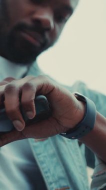 Günlük kıyafetli bir adam akıllı saatini kontrol ediyor, teknoloji ve yaşam tarzının kaynaşmasını vurguluyor..